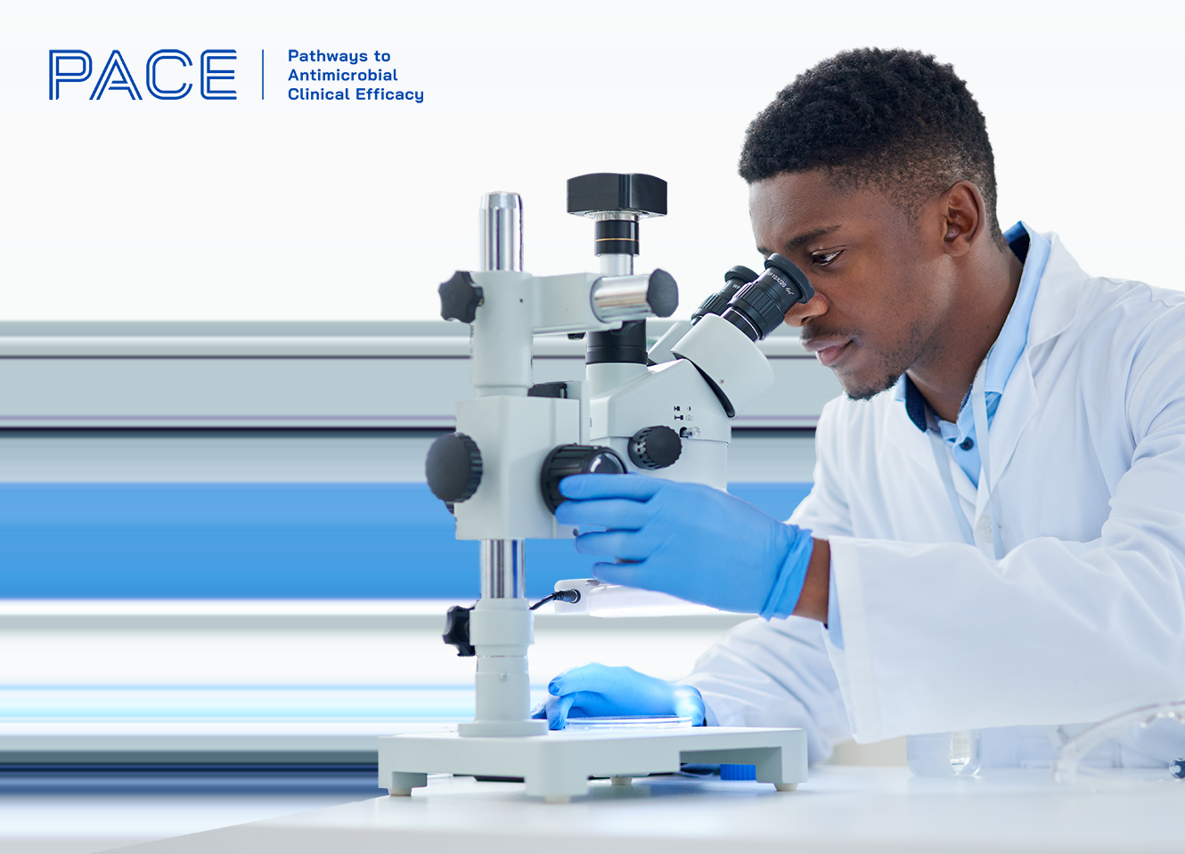 A black male scientist wearing PPE is looking through a microscope