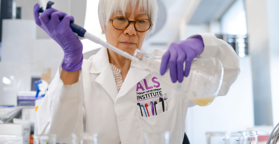 female scientist wearing glasses pipetting liquid into a conical flask